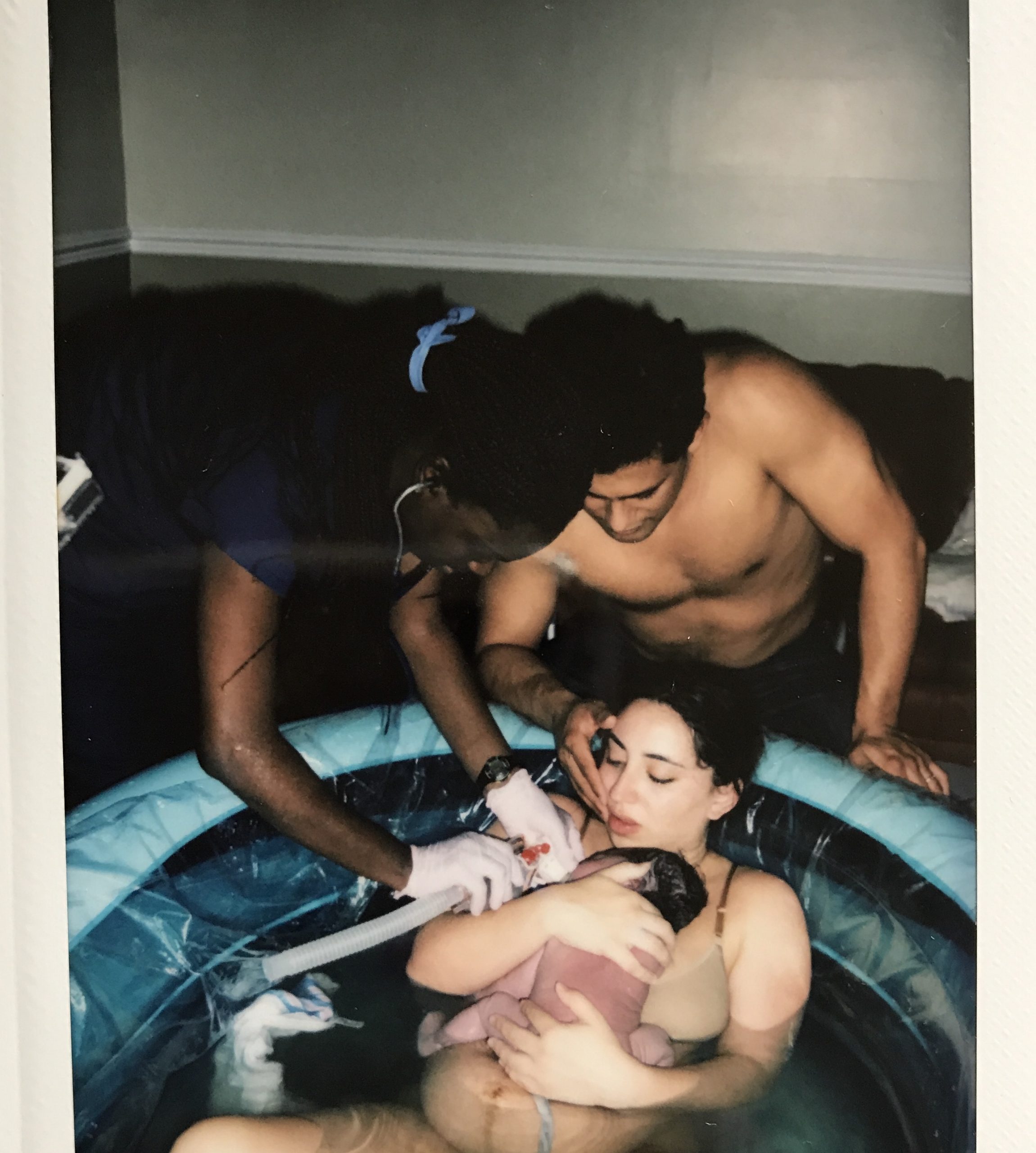 midwife giving oxygen to baby in birth pool with mother and father