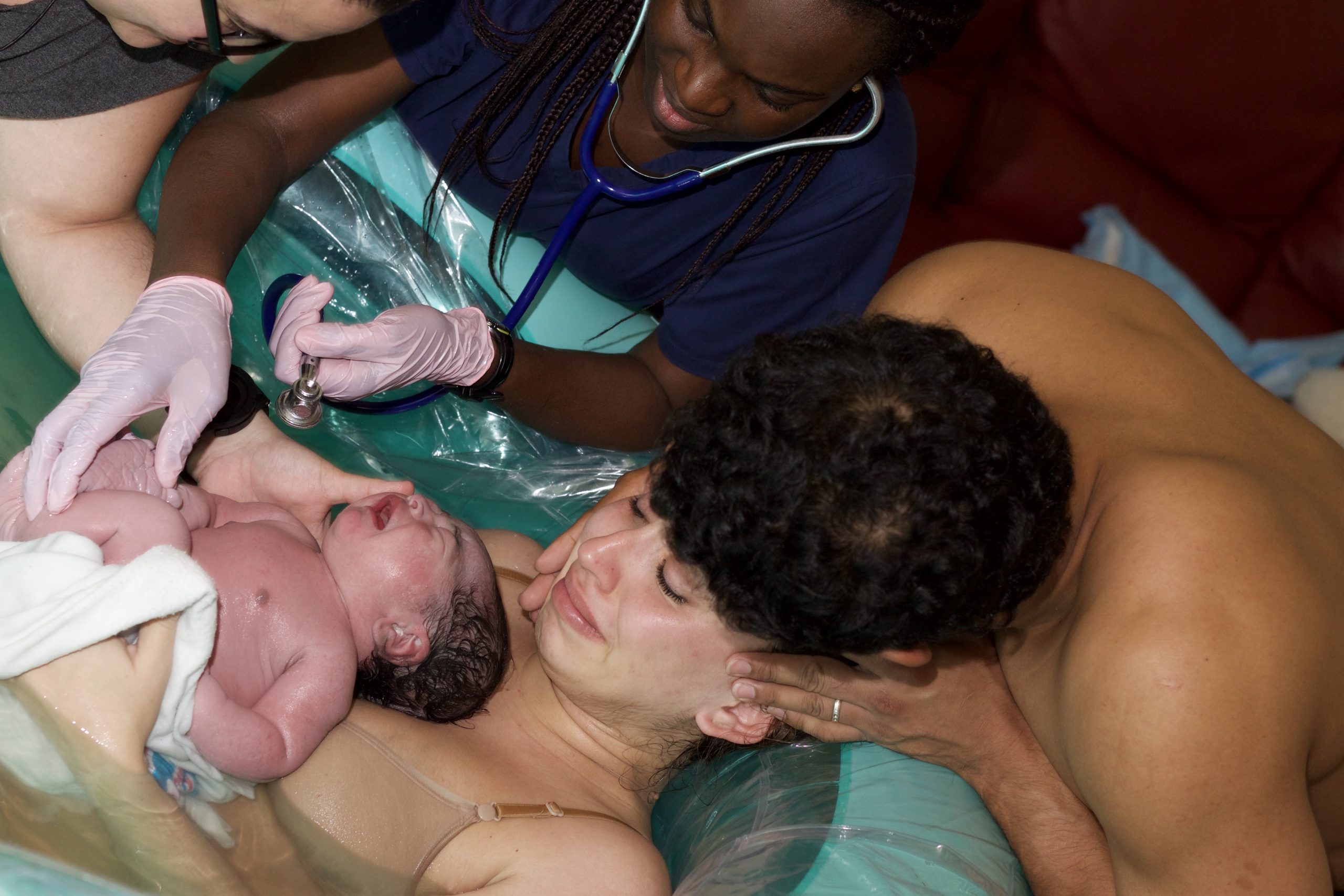 father holds mother face after birth in birth pool with baby
