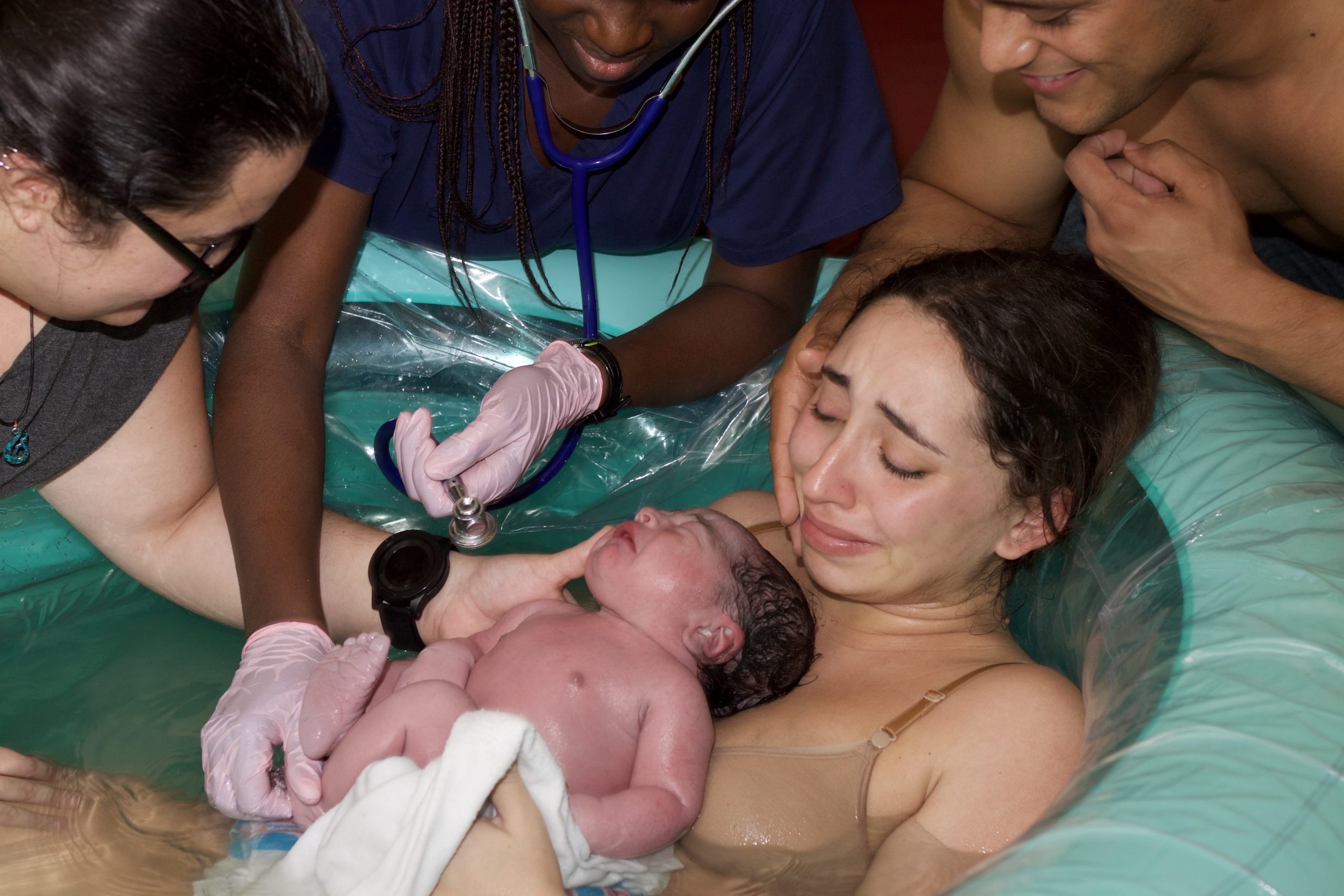mother and baby in birth pool surrounded by midwives