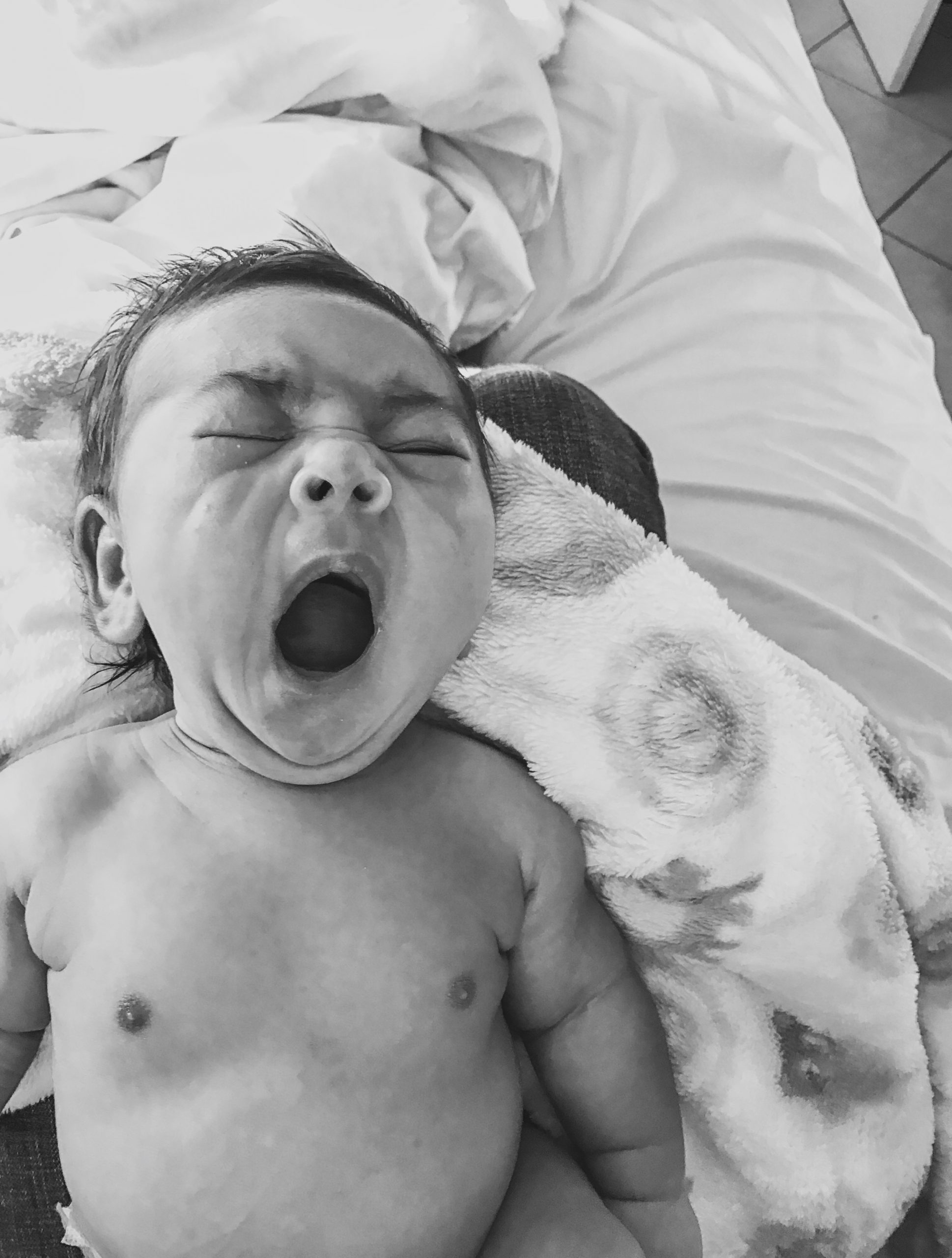 greyscale image of baby yawning laying on bed