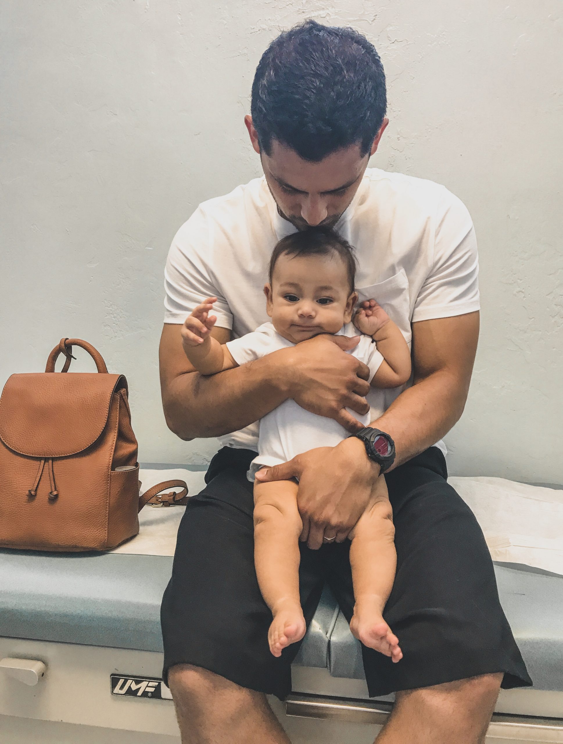 baby being held by father in doctors office getting first vaccines