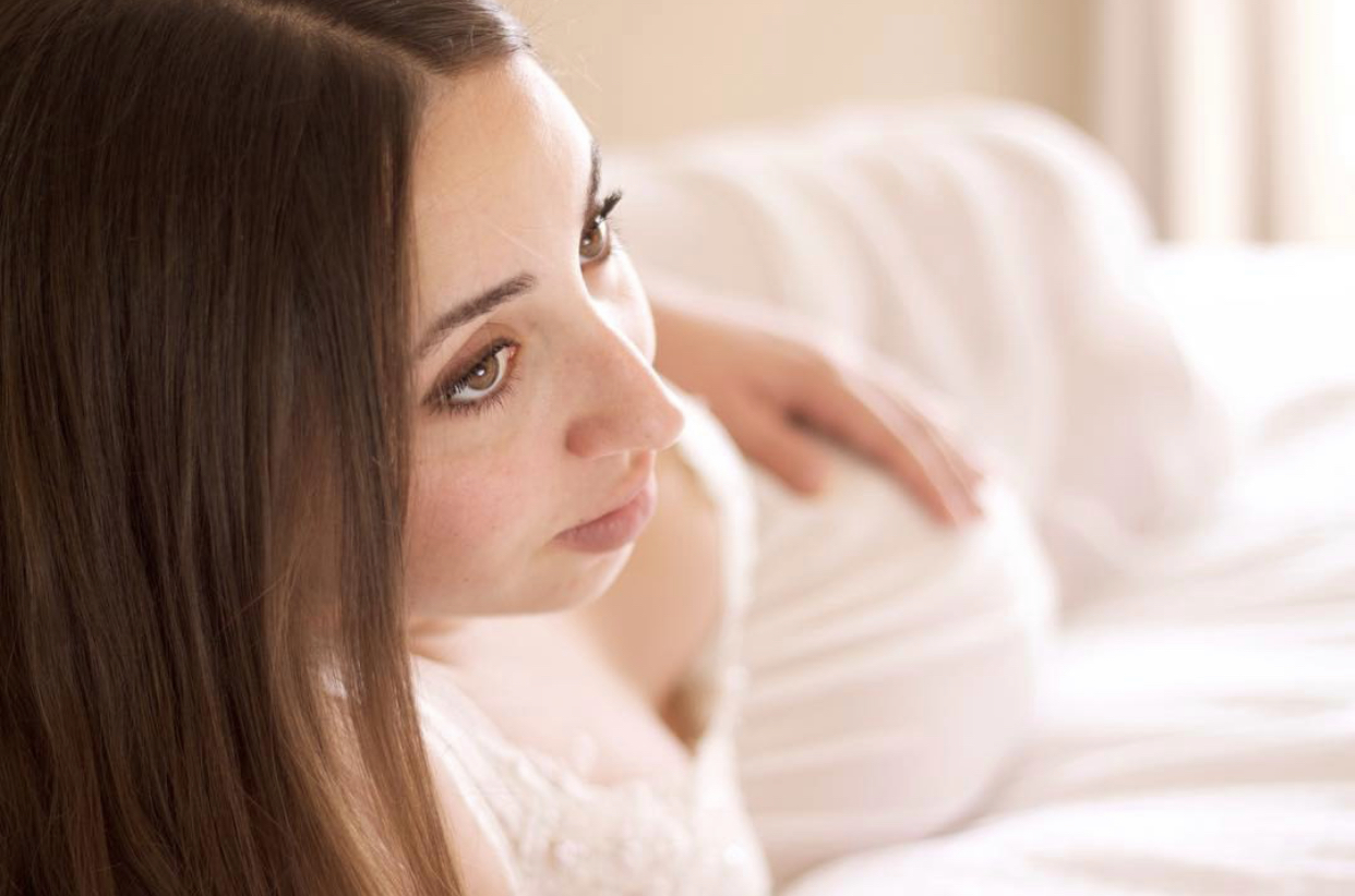 pregnant woman laying on bed holding belly looking out